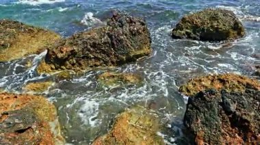 Açık mavi deniz suyu kayalık sahili yıkar. Okyanus kıyısında büyük taşlar. Dalgalar kıyıdaki kayalıklara çarpıyor..