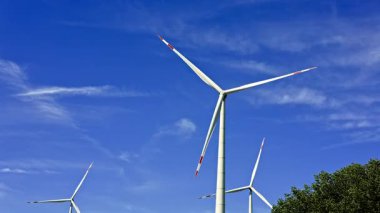 Mavi gökyüzüne karşı büyük rüzgar türbinleri. Yel değirmenleri döner ve temiz enerji üretir. Büyük yel değirmenleri ve inanılmaz bulutlu mavi bir gökyüzü..