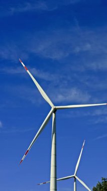 Mavi gökyüzüne karşı yel değirmenlerinin dikey videosu. Rüzgar türbinleri bir alanda dönüyor ve enerji üretiyor. Alternatif enerji üretimi.