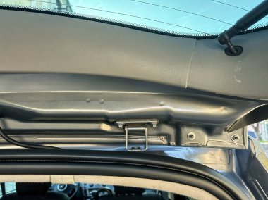 Açık bir günde park halindeki bir aracın yapı ve işlevselliğini vurgulayan, parlak güneş ışığı altında bir arabanın iç çatı çerçeve ve mandal sisteminin yakın görüntüsü.