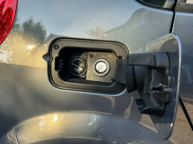 Yakından bakıldığında elektrikli bir aracın şarj portunu gösteriyor, arabanın pürüzsüz gri yüzeyinden yansıyan güneş ışığı bağlantı noktasını ortaya çıkarıyor..