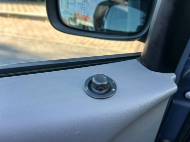 Yakından bakıldığında, yan aynayı ayarlamak için bir kontrol düğmesi görünür, bir araba kapısının pürüzsüz yüzeyine göre ayarlanır. Güneş ışığı dışarıdaki sakin banliyö caddesini aydınlatıyor.