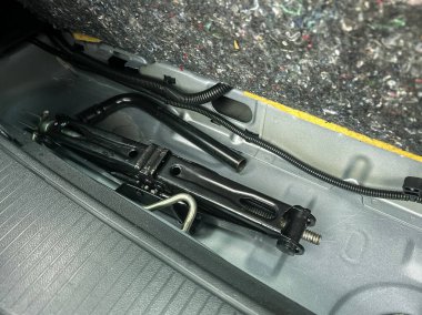 Bir arabanın bagajının içini incelemek halı astarının altına yerleştirilmiş siyah bir kriko ortaya çıkardı. Seyahat maceraları sırasında acil yardım için hazırdı..