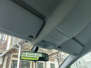 Arabanın iç tarafının, tavan, güneş gözlüğü ve dikiz aynasını gösteren yakın çekim görüntüsü, şehir manzarasının arka planıyla günlük detayları vurguluyor..