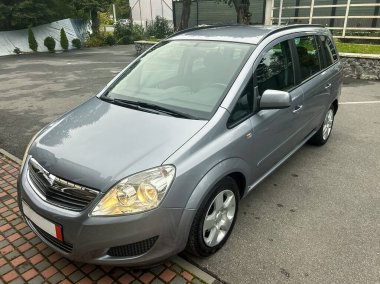 Modern bir gümüş aile aracı düzgün asfalt bir alanda duruyor. Etrafı yeşilliklerle çevrili. Pürüzsüz tasarımı ve parlak günışığında parlak alaşımlı tekerlekleri sergiliyor..