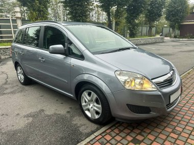 Pürüzsüz bir tuğla yolda park etmiş parlak gümüş renkli bir araba. Yeşillik ağaçlar caddeyi kaplıyor ve bulutlu gökyüzü yaklaşan yağmurun huzurlu bir atmosfer yarattığını ima ediyor..