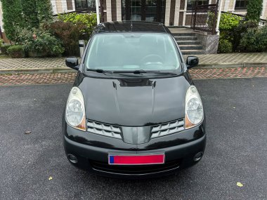 Gösterişli siyah bir araç yeşilliklerle çevrili modern bir binanın önünde gururla duruyor. Sahne huzurlu bir anı yakalıyor, arabanın parlak yüzeyini gösteriyor ve tasarımı davet ediyor..