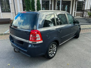 Parlak gri bir minivan, geniş pencereli çağdaş bir yapının önüne park edilmiştir. Huzurlu manzara bulutlu bir öğleden sonranın cazibesini yakalar..