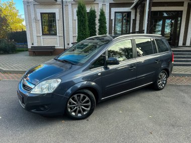 Güzel, modern bir yapının yanına park edilmiş şık bir aile arabası. Güneş ışığı sahneyi aydınlatıyor, arabanın parlak tasarımını ve ağaçların gür arka planını vurguluyor..