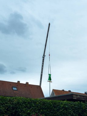 Çatıların üzerinde büyük bir vinç kulesi, önemli bir nesneyi dikkatlice kaldırıyor. Üstümüzde kara bulutlar belirdi. İnşaat çalışmaları devam ederken muhtemel yağmura işaret ediyor..