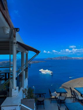 Misafirler, Yunanistan 'ın Santorini kentindeki parlak bir gökyüzü altında derin mavi sularda seyreden ve manzaralı tepelerle çevrili beyaz bir yolcu gemisinin keyfini çıkarıyorlar..