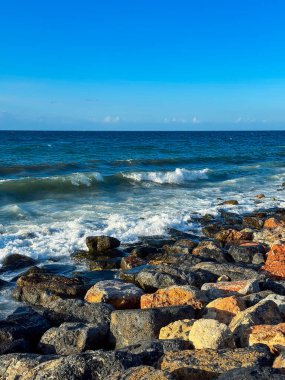 Dalgalar, canlı taşların mavi okyanusa karşı güzel bir kontrast oluşturduğu kayalık bir kıyı şeridine nazikçe yaklaşarak doğada huzur hissi uyandırır..