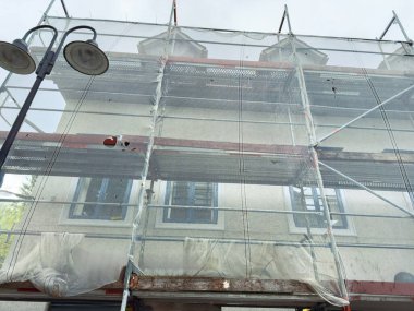 İşçiler titizlikle iskeleye sarılı klasik bir yapıyı koruyorlar. Bulutlar tepemizde toplanırken cazibesini korumaya odaklanıyorlar. Daha sonra yağmur yağma ihtimalini işaret ediyorlar..