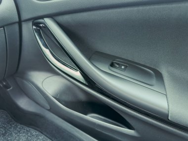 Bir arabanın iç kapısında modern estetikle karıştırılmış şık bir kapı kolu ve güçlü bir pencere anahtarı sergileniyor. Yumuşak güneş ışığı parlak yüzeyleri ve dokuları vurgular.