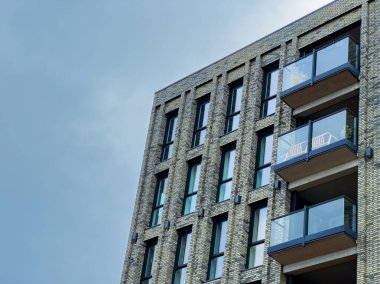 Çağdaş bir apartman dairesi parlak mavi bir gökyüzünün altında, sakinlerin keyif almaları için manzaralar ve açık alanlar sunan geniş balkonlarla ayakta duruyor..