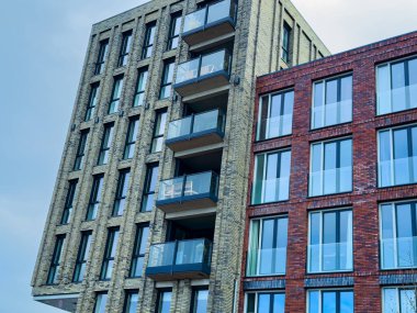 Benzersiz bir bina, açık bir gökyüzü altında geniş cam pencereler ve geniş balkonların yer aldığı yeşil ve kırmızı tuğlalardan oluşan karmaşık bir karışım sergiliyor..