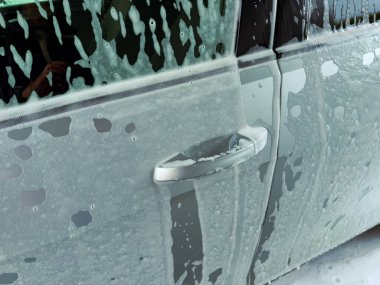 Köpükler arabanın kenarını tamamen yıkarken güneş ışığı sabundan yansıyarak ışıl ışıl bir etki yaratıyor. Şehir hayatı bu anı sarmış durumda..