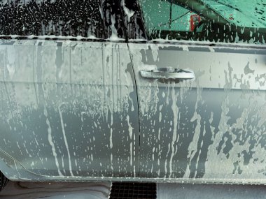 Köpüklü köpüklü köpükler parıldayan gümüş bir arabadan aşağı yuvarlanırken yoğun bir araba yıkama sırasında temiz ve parlak bir görünüm yaratır. Parlak güneş ışığı canlı renkleri vurgular ve ıslak yüzeylerden yansıtır..