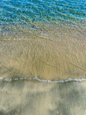 Yumuşak dalgalar kumlu sahili öperken, berrak sularda gün ışığı parıldıyor. Huzurlu bir sahile bir dinlenme ve yansıma anı davet ediyor..