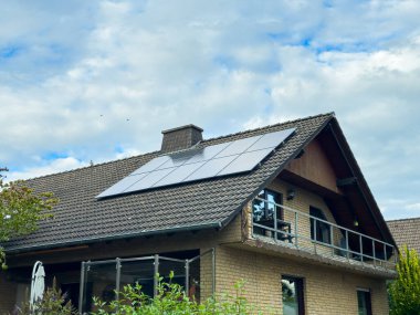 Konforlu bir ev çatıda güneş panelleri sergiliyor. Çevre dostu teknolojiyi geleneksel mimari ile harmanlayarak dağınık bulutların oluşturduğu bir zemin oluşturuyor..