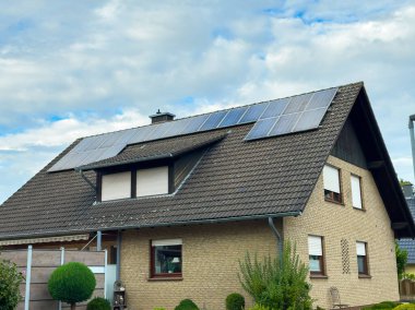 Çatı güneş panelleri yumuşak güneş ışığı altında parlıyor. Yeşil çalılarla çevrili büyüleyici bir evde çevreci çevre dostu enerji kullanımı sergiliyorlar..