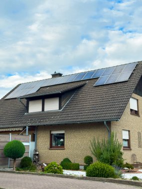 Çağdaş bir evde, çatısı iyi korunmuş bahçeler ve çalılarla çevrili güneş panelleri bulunur. Parlak gökyüzü sıcak öğleden sonra atmosferine huzur katıyor..