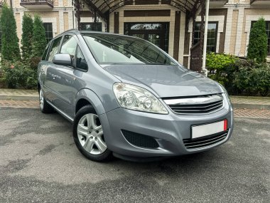 Parlak gümüş renkli bir minivan yemyeşil ile çevrili büyüleyici bir tuğla yapının önüne park edilmiş. Sahne bulutlu bir gökyüzü ile huzurlu bir anı yakalar..