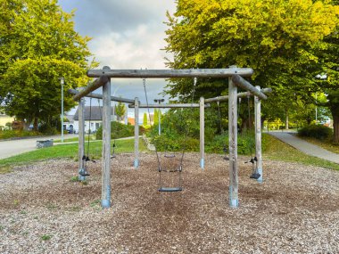 Huzurlu bir oyun alanı sahnesinde, dramatik bir gökyüzünün altında canlı sarı ağaçlarla çevrili, yavaşça sallanan boş salıncaklar yer alır. Bu öğleden sonra eğlence ve kahkaha potansiyeli ile dolu..