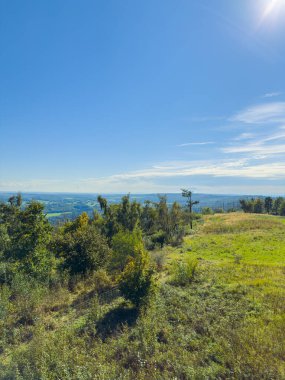 Yükselmiş bakış açısına göre, kırsal alan yeşillik ve kayalık arazinin bir karışımını sergileyerek çok geniş bir alana yayılıyor, açık mavi gökyüzü ise keşif ve dinginliği davet ediyor..