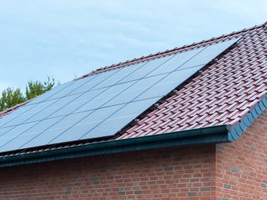 Sakin bir öğleden sonra, bir evin çatısı parlak güneş panelleriyle süslenir, yeşil enerjide yenilik sergiler. Bulutlu gökyüzü bugünün sürdürülebilirlik gelişimine işaret ediyor..