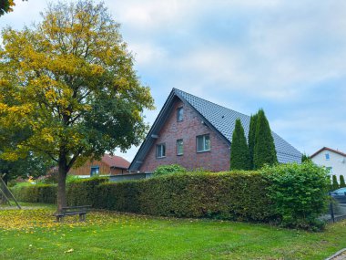 Sakin bir ortamda, sakin bir tuğladan ev duruyor, güzel bir çitle çevrili ve bulutlu bir gökyüzünün altında altından yaprakları olan canlı bir ağaç, sakin bir sonbahar öğleden sonrasını çağrıştırıyor..