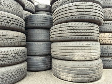 Bir araba hurdalığında duran istiflenmiş lastik koleksiyonu öğleden sonra güneş ışığını yakalıyor. Eskimiş tasarımlar ve çeşitli boyutlar ilginç bir görsel ekran oluşturur.