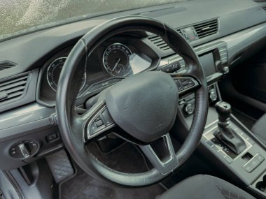 Şık bir arabanın içinde siyah bir direksiyon ve modern gösterge paneli bulunur. Yağmurlu bir günde hafif ışıklandırma sürücüler için sakin bir atmosfer yaratıyor..