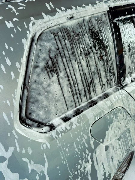 Sabun köpükleri parlak, gümüş renkli bir arabayı kaplıyor. Suyun yanından aktığı neşeli bir sahne yaratıyor. Güneşli bir ortamda araba temizlemenin canlı bir öğleden sonrasını sergiliyor..