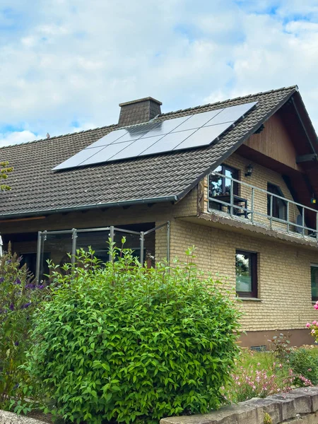Büyüleyici bir evin çatısında verimli yeşillikler ve mükemmel manikürlü bir bahçeyle çevrili güneş panelleri bulunur. Sahne, mavi gökyüzünün altında sakin, çevre dostu bir ortam yakalıyor..