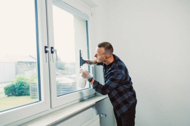 Çağdaş bir odada pencereyi özenle temizleyen bir adam, içeri güneş ışığı giriyor. Sahne, temiz bir evin ve temiz havanın önemini vurguluyor..