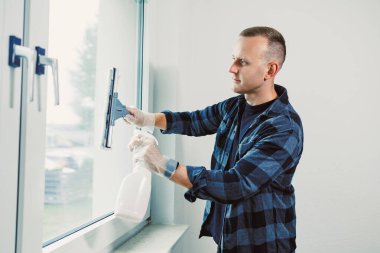 Kareli gömlekli bir adam cam sileceği ile pencereyi temizlemeye odaklanır. Parlak ışık, camı bir çözelti ile doldurarak, temiz bir görüş sağlar..