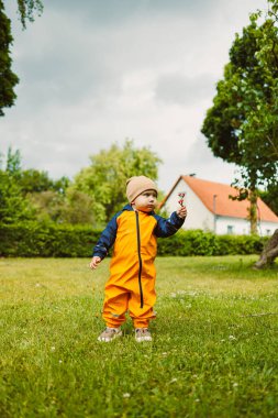 Genç bir çocuk renkli turuncu bir elbise giymiş, elinde sopayla yemyeşil bir bahçe keşfediyor. Sahne, huzurlu bir ortamda neşeli bir ruh yakalar..