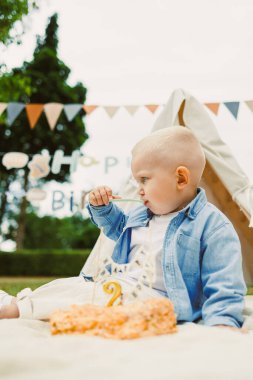 Neşeli bir çocuk, neşeli süslemeler ve çadırlarla çevrili bir bahçede, canlı bir doğum günü kutlamasının tadını çıkarıyor. Lezzetli bir ziyafetin tadını çıkarıyor..