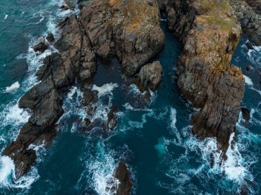 Dalgalar engebeli kayalara çarparak sakin bir kıyı bölgesinde dinamik bir manzara yaratır. Güneş doğar, sıcacık bir ışık yayar ve doğanın güzelliğini arttırır..