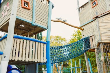 Ağaçların arasında yuva yapmış renkli bir oyun alanını keşfederken çocukların kahkahaları havayı dolduruyor. Yükselen yapılar, parlak gökyüzünün altında tırmanmaya, kaymaya ve yaratıcı oyunlara davetiye çıkarır..