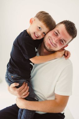 Neşeli bir baba ve oğlu, yakın ilişkilerinin sıcaklığını gösteren sevgi dolu bir kucaklaşmayı paylaşıyor. Parlak ve davetkar bir stüdyo ortamında güzelce aydınlatılıyor.