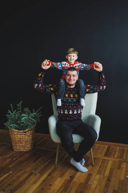 Yürek ısıtan bir görüntü, renkli tatil kazaklarıyla oğluyla bağ kuran bir babanın hoş bir ortamda neşe ve bağlantı yakaladığını gösteriyor. Şenlik teması için mükemmel.