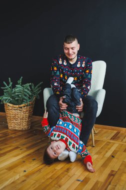 Sıcak, kapalı bir ortamda neşeli bir baba ve oğlu neşeli bir tatil süveteri giyerken keyifli bir anı paylaşıyor. Eğlencelerini, sevgilerini ve ilişkilerini sergiliyorlar.
