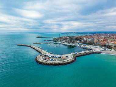 Suya yanaşmış birkaç teknesi olan bir marina. Kıyı şeridi boyunca binalar var. Gökyüzü bulutlu, bulutlu bir günü işaret ediyor..