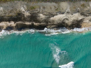 Okyanustan gelen su kıyıya vurur, kumlu sahile ve kayalık kayalıklara vuran dalgalar yaratır. Sahne açık gökyüzü ile aydınlık bir gün ortasını yakalıyor..