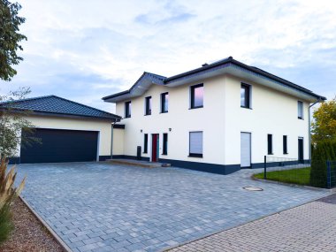 Banliyö ortamında büyük bir ev duruyor. Binanın bir garaj ve garaj yolu var. Pencerelere yansıyan ışıkta gökyüzü akşam renklerini gösterir.