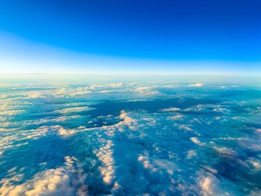 Bir uçak okyanusun üzerinde yüksek uçuyor. Bulutlar mavi ve beyaz tonlarıyla gökyüzüne yayıldı. Güneş ışığı akşam yaklaştıkça değişmeye başlar ve güzel bir sahne yaratır..