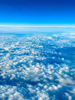 Uçaktan bir görüntü, okyanusun üzerindeki mavi gökyüzüne yayılmış beyaz bulutları gösteriyor. Sahne, gün ortasında gökyüzünün enginliğini ve güzelliğini yakalar..