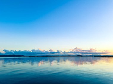 Su uzak bir arazinin üzerinde yüzen bulutlar gibi gökyüzünün renklerini yansıtır. Sahne, gece gündüz göldeki geçişi akşam saatlerinde yakalıyor..
